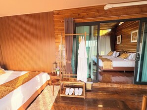 A room with wooden walls, a bed with white bedding, a small table with a lamp, and a shoe rack.