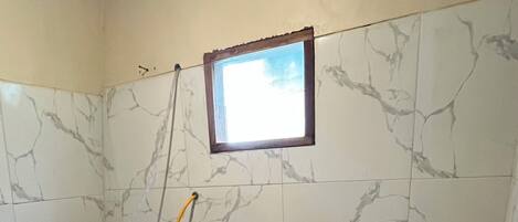 A small bathroom with a toilet, a shower, and a window.