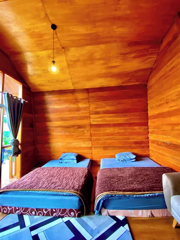 A wooden cabin room with two beds, a hanging light fixture, and a view of the outdoors through a window. - Villa Ira Dieng (Dieng Kulon)