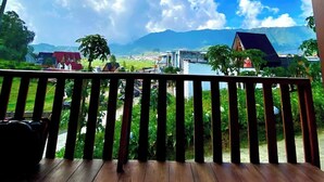 Una terraza de madera con vistas a un río, montañas y casas a lo lejos.