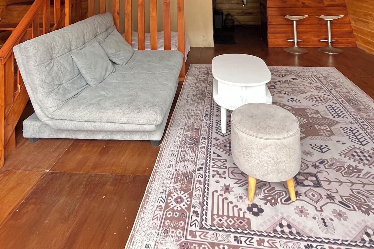 Um quarto de sótão aconchegante com escada de madeira, sofá, mesinha e tapete estampado.