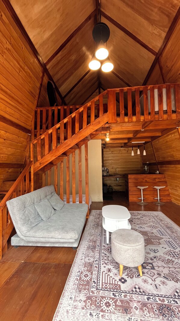 Une pièce mansardée chaleureuse, avec un escalier en bois, un canapé, une petite table et un tapis à motifs.