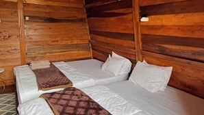 Habitación de cabaña de madera con dos camas, cada una con ropa blanca y una manta marrón.