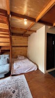 A room with wooden walls and ceiling, a bed with white bedding, a grey sofa, and a patterned rug.