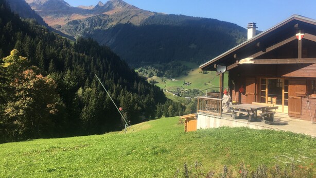 A mountain lodge with a wooden exterior, a balcony with outdoor seating, and a view of the surrounding mountains and valley. - Infinitely mountainous atmosphere, ski in/ski out chalet in Arêches Beaufort (Beaufort)