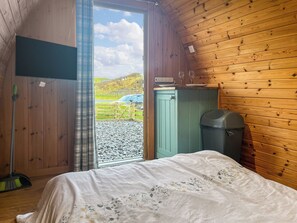 A room with a bed, a wooden cabinet, a trash bin, and a view of a green field through a door. - Birds pod is the perfect place for up to two guests to reconnect with nature. (Dalton-in-Furness)