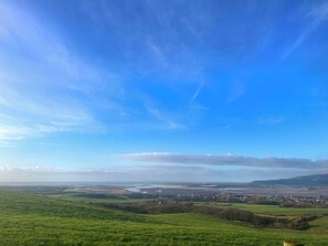 A panoramic view of a green landscape with a clear sky and distant buildings.