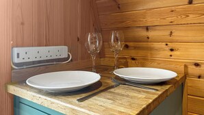 A wooden interior with a wooden countertop, two white plates, a fork, a knife, and two wine glasses. - Birds pod is the perfect place for up to two guests to reconnect with nature. (Dalton-in-Furness)