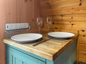 A wooden interior with a wooden countertop, two white plates, a fork, a knife, and two wine glasses.