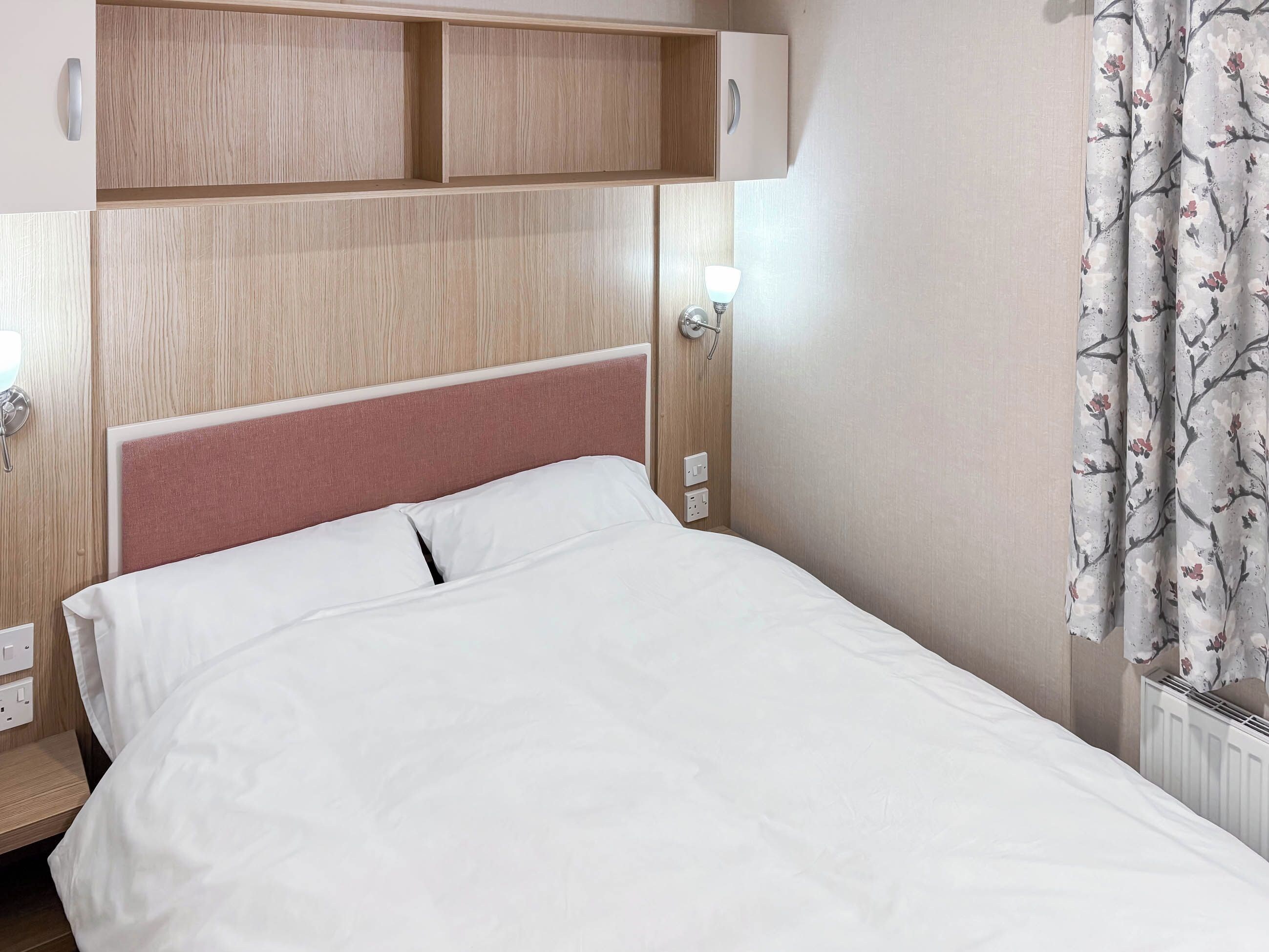 A neatly made bed with white linens, a wooden headboard, and a wall-mounted light fixture.