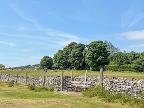 Ländliche Landschaft mit Steinmauer, Holzbank und Schaukel.