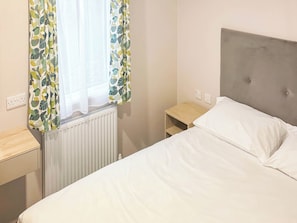 A bedroom with a bed, a nightstand, a radiator, and a window with curtains.