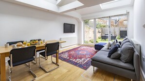Ein modernes Wohnzimmer mit Essbereich, einer Couch, einem Fernseher und Blick auf den Garten.