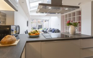 A modern kitchen with a central island, a dining area with a sofa, and a view of the backyard through large windows. - The Jericho Retreat | Oxford Holiday Let | 4 Beds & Sleeps 8 (Oxford,)