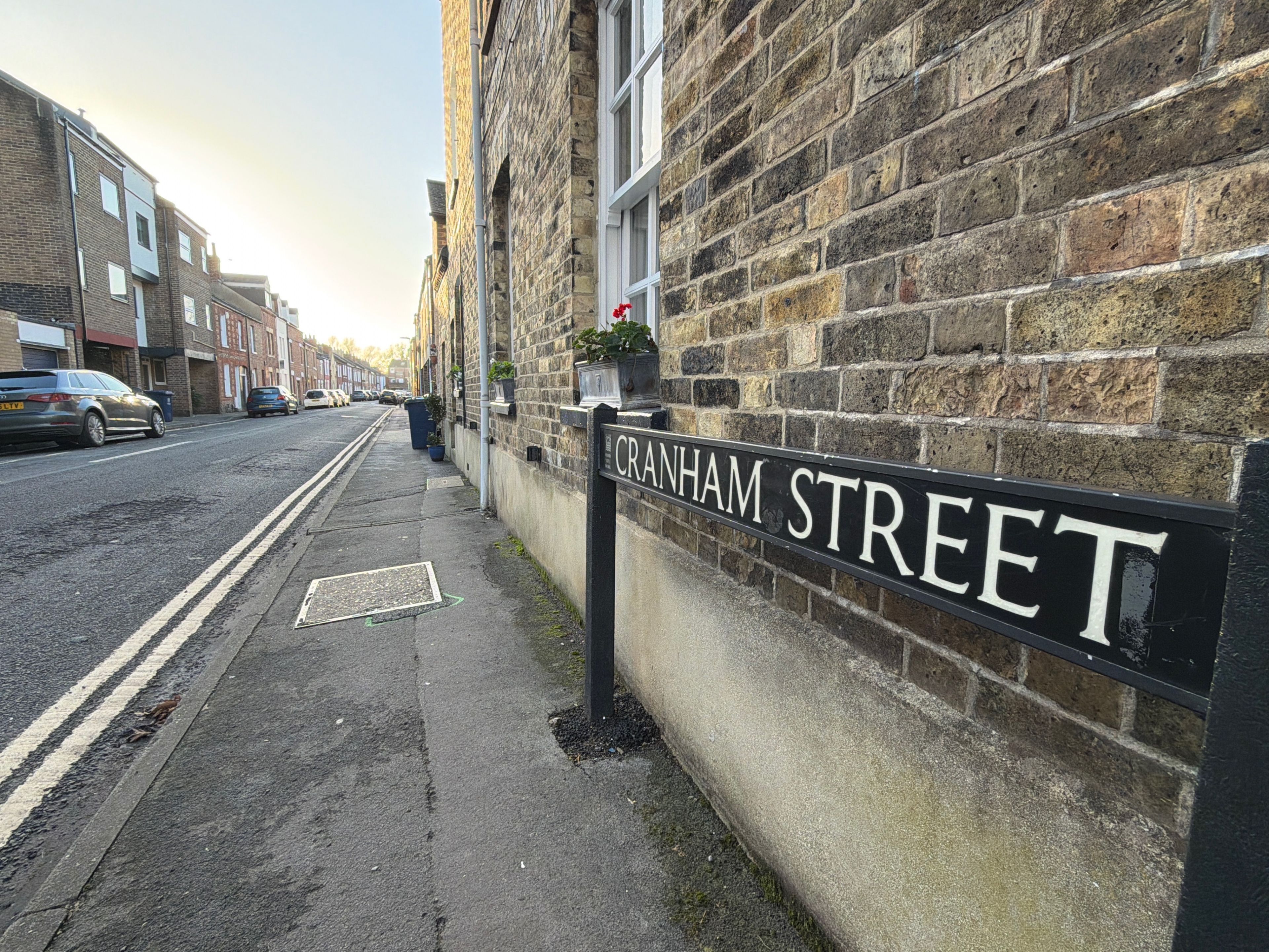 A street sign for Cranham Street, adjacent to a building with a stone facade and a parked car.