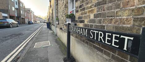 A street sign for Cranham Street, adjacent to a building with a stone facade and a parked car.