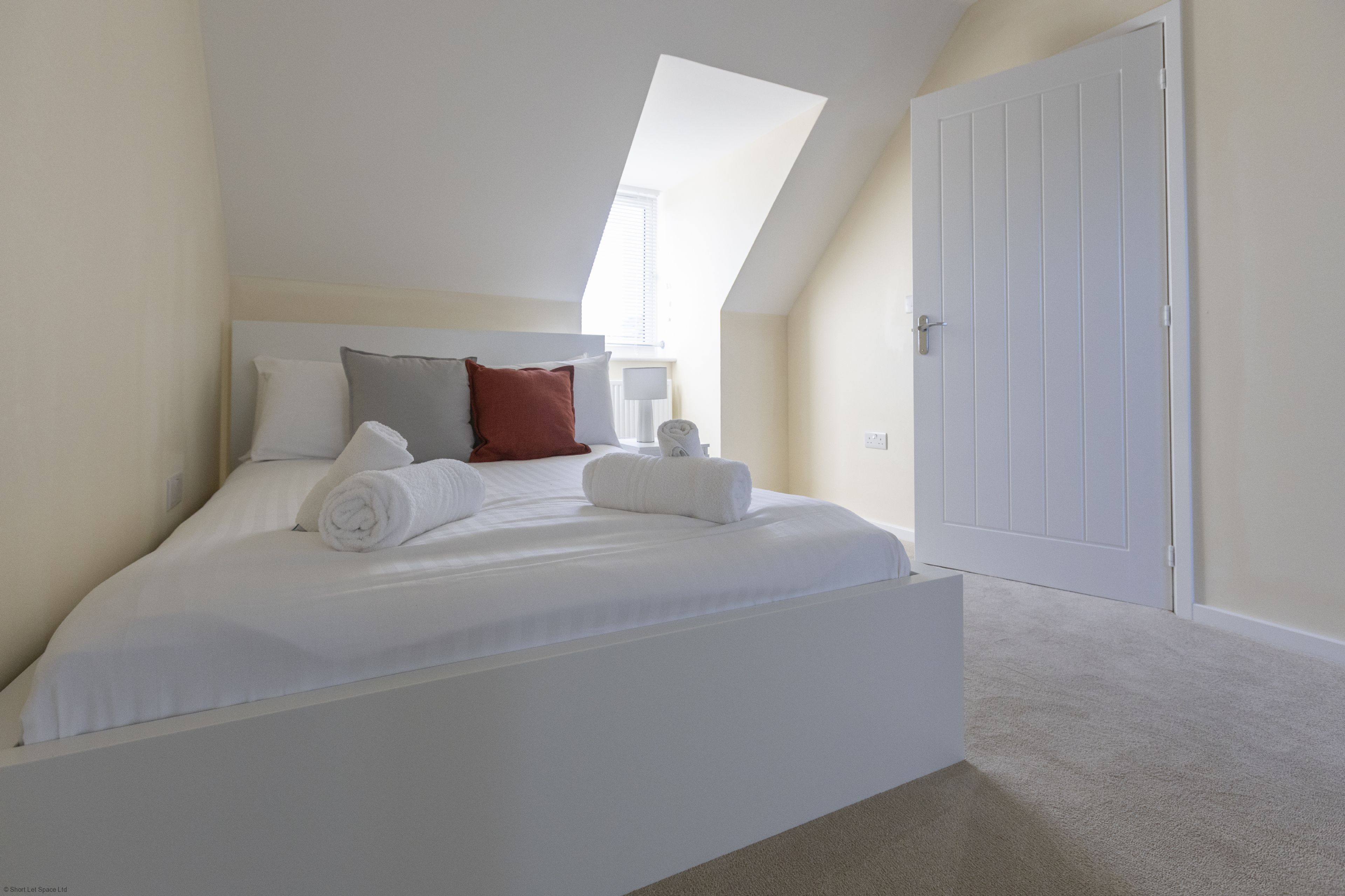 Quarto com cama, almofadas, mesa de cabeceira e porta.