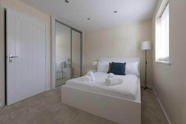 A bedroom with a bed, a bedside table, a lamp, a sliding door, and a window with blinds.