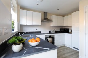 A modern kitchen with white cabinets, a black marble countertop, a built-in oven, and a microwave.