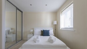 Un dormitorio moderno con una cama grande, una mesita de noche, una lámpara y un ventanal corredero que da al baño.