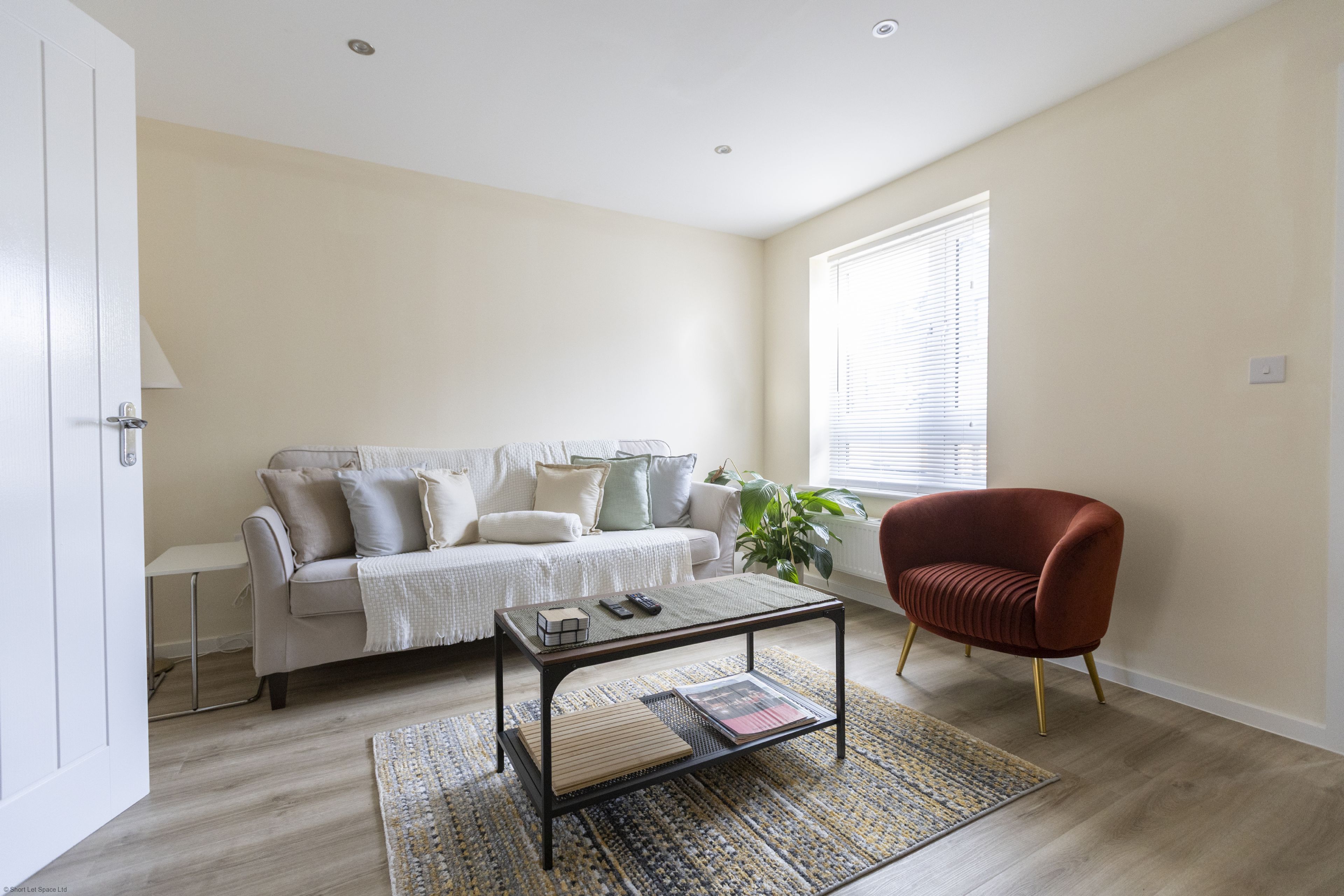 A living room with a sofa, a coffee table, a red armchair, and a window with blinds.