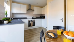 Una cocina moderna con armarios blancos, encimera negra y una mesa de comedor de madera con un croissant y jugo de naranja.