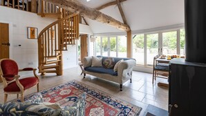 Een ruime woonkamer met een houten trap, een bank, een rode fauteuil en een groot raam met uitzicht op de omgeving.
