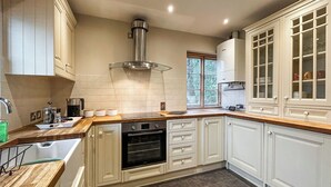 A kitchen with white cabinetry, a built-in oven, a stainless steel range hood, and a window with blinds. - 4 bedroom accommodation in Sutton Coldfield (Sutton Coldfield)