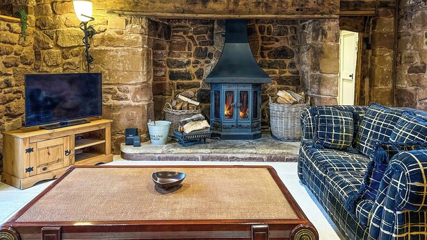 A rustic room with a stone wall, a fireplace, a television, and a sofa. - 4 bedroom accommodation in Sutton Coldfield (Sutton Coldfield)