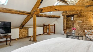 A bedroom with a large bed, a television, a stone wall, and a wooden ceiling structure. - 4 bedroom accommodation in Sutton Coldfield (Sutton Coldfield)