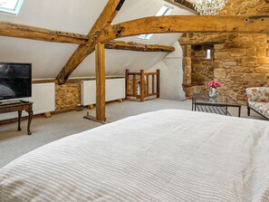 A bedroom with a large bed, a television, a stone wall, and a wooden ceiling structure.