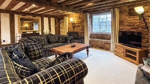 A cozy living room with a large sofa set, a wooden coffee table, and a stone fireplace. - 4 bedroom accommodation in Sutton Coldfield (Sutton Coldfield)