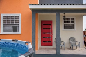 Una piscina, una puerta roja y dos sillas Adirondack frente a un edificio.