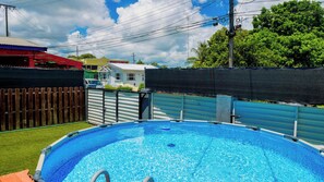 Una piscina con valla de madera, portón metálico y una casa al fondo.