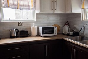 Una cocina con microondas, tostadora y hervidor en la encimera, un lavabo y armarios.