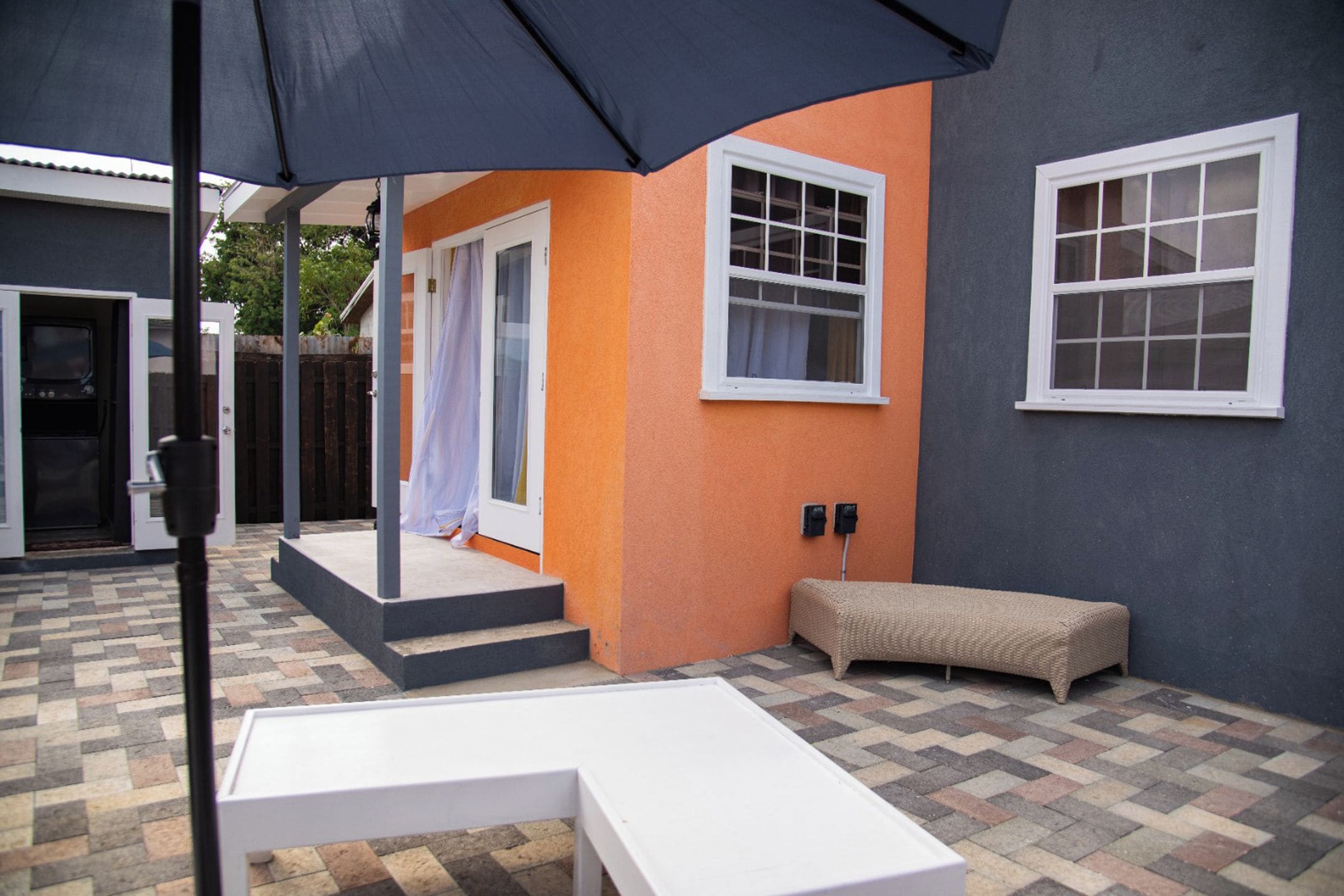 Un espace patio avec une table blanche, un banc et un coin salon abrité.
