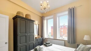 A bedroom with a large bed, a wardrobe, a window with curtains, and a chandelier. - 1 bedroom accommodation in Whitby (Whitby)