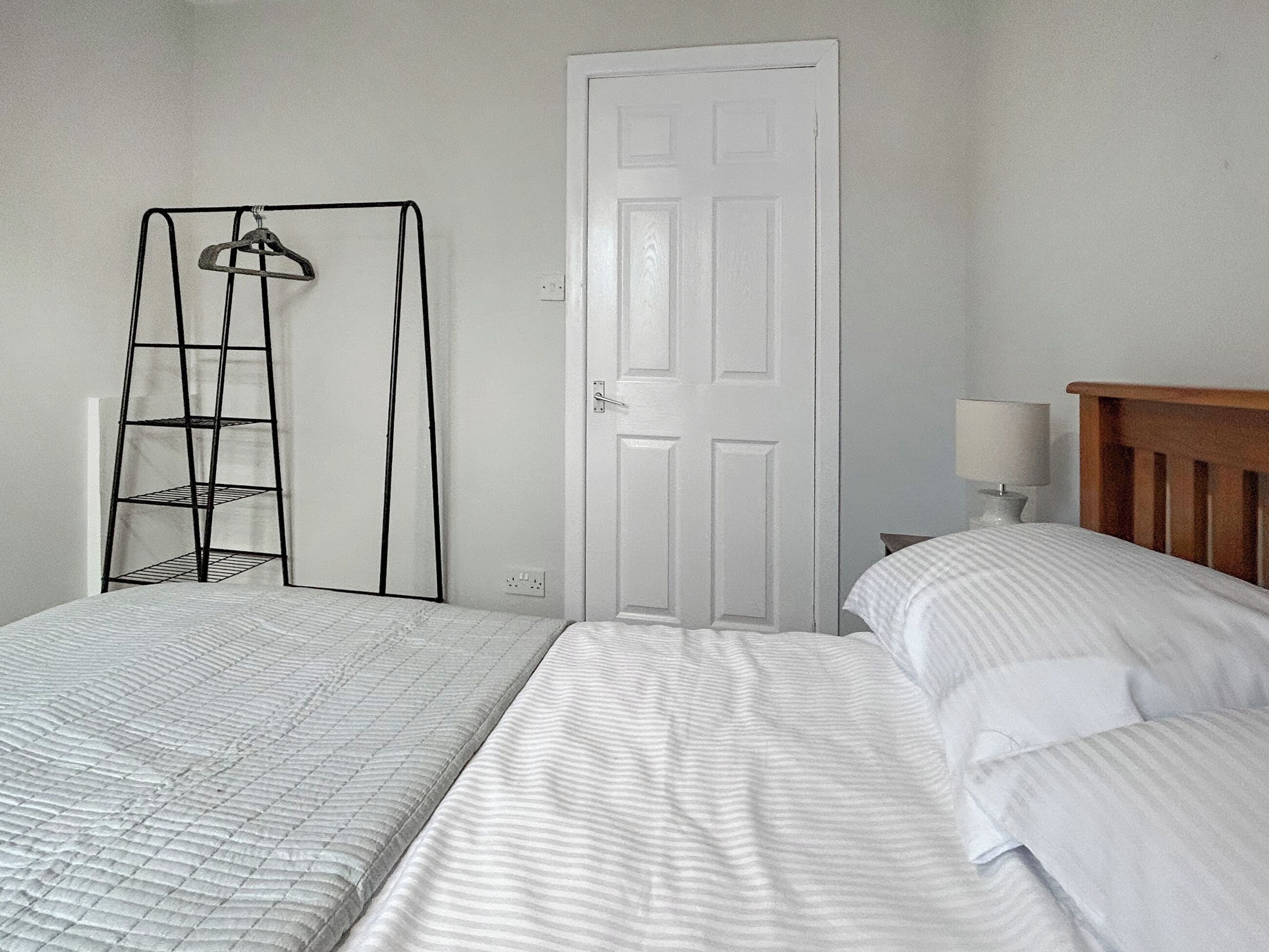 Une chambre avec deux lits, une porte blanche, une table de chevet avec une lampe et une étagère en métal.