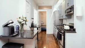A narrow kitchen with a central island, a microwave, oven, and a kettle. - Prime East Village Two Bedroom (New York)