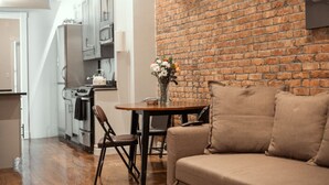 A kitchen with a brick wall, a dining table with chairs, and a sofa. - Prime East Village Two Bedroom (New York)