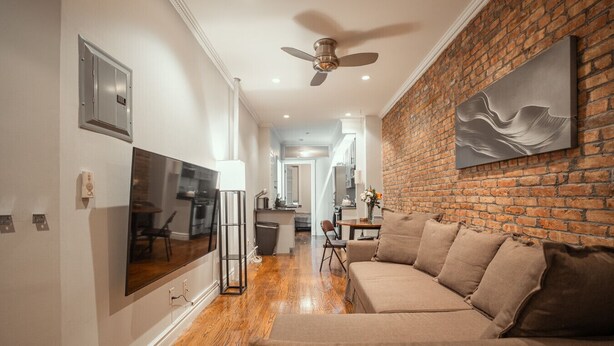A modern living room with a brick wall, a ceiling fan, and a large flat-screen TV. - Prime East Village Two Bedroom (New York)