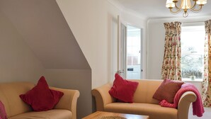 Ein gemütliches Wohnzimmer mit zwei beigefarbenen Sofas, jeweils mit einem roten Kissen, und einem Holztisch mit gewebten Untersetzern.