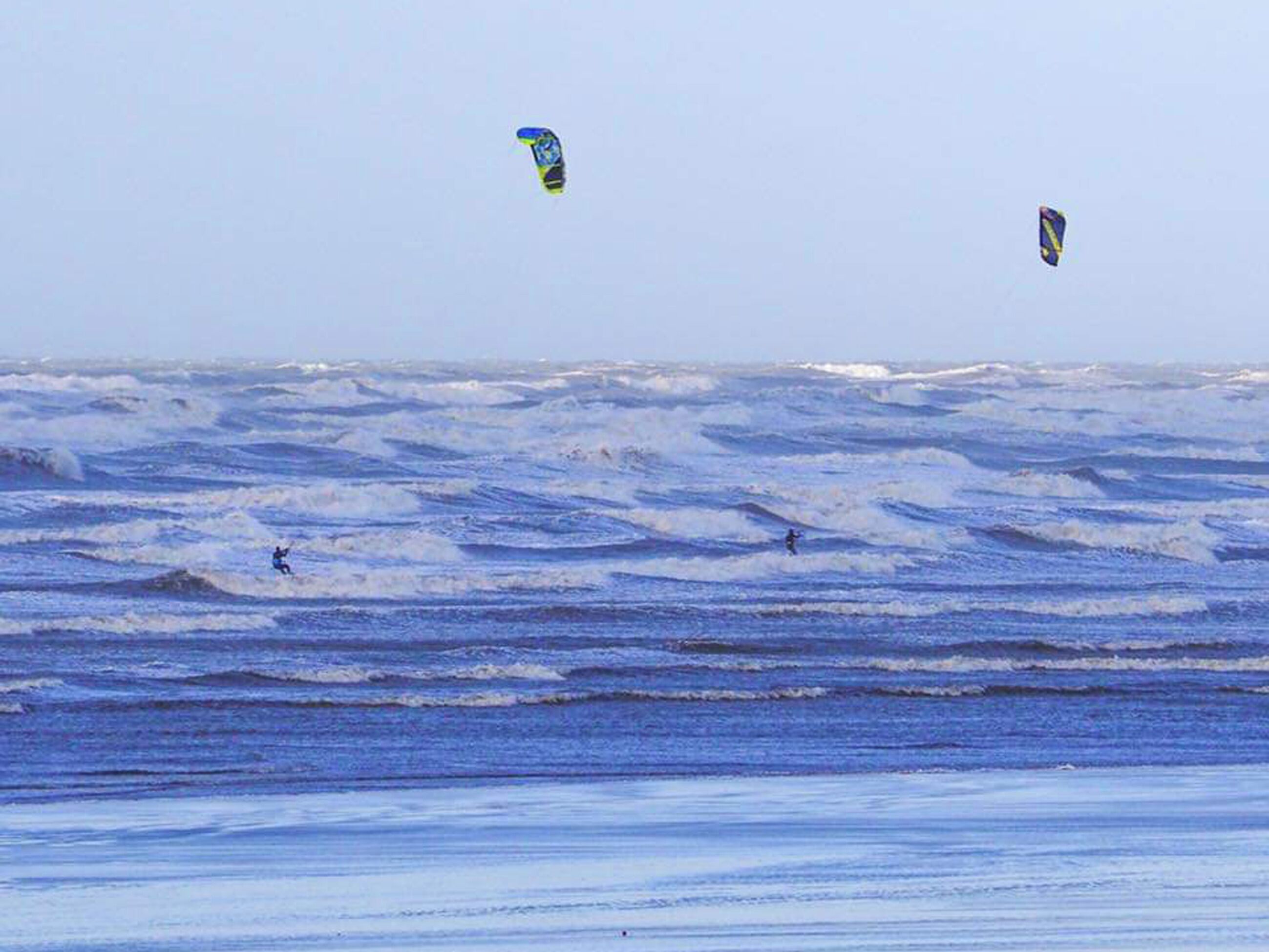 Une plage avec des vagues et des gens qui font de la planche à voile.