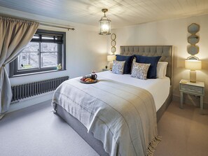 A bedroom with a large bed, a bedside table, a nightstand, a window with curtains, a radiator, and a hanging light fixture. - 1 bedroom accommodation in Guisborough (Guisborough)