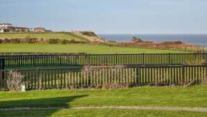 Un paysage côtier avec une zone herbeuse, une clôture en bois et des maisons en arrière-plan.