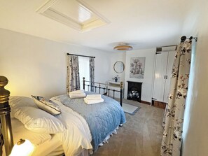 Ein Schlafzimmer mit Bett, Nachttisch, Spiegel, Kamin und Vorhängen.