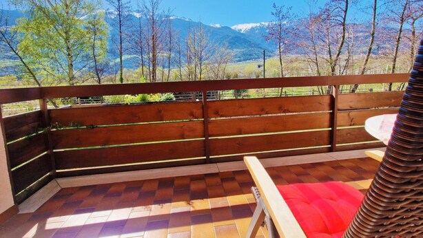 Un balcon avec une balustrade en bois, un sol à carreaux et un fauteuil rouge avec coussin.