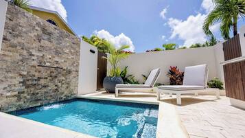 A swimming pool with two lounge chairs and a potted plant.