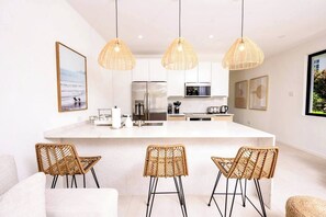 A modern kitchen with a central island, wicker chairs, and pendant lights. - Azzurro Townhouses - by Zenbreak (Speightstown)
