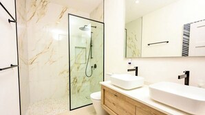 A modern bathroom with a glass-enclosed shower, a white toilet, and a wooden vanity with two sinks. - Azzurro Townhouses - by Zenbreak (Speightstown)